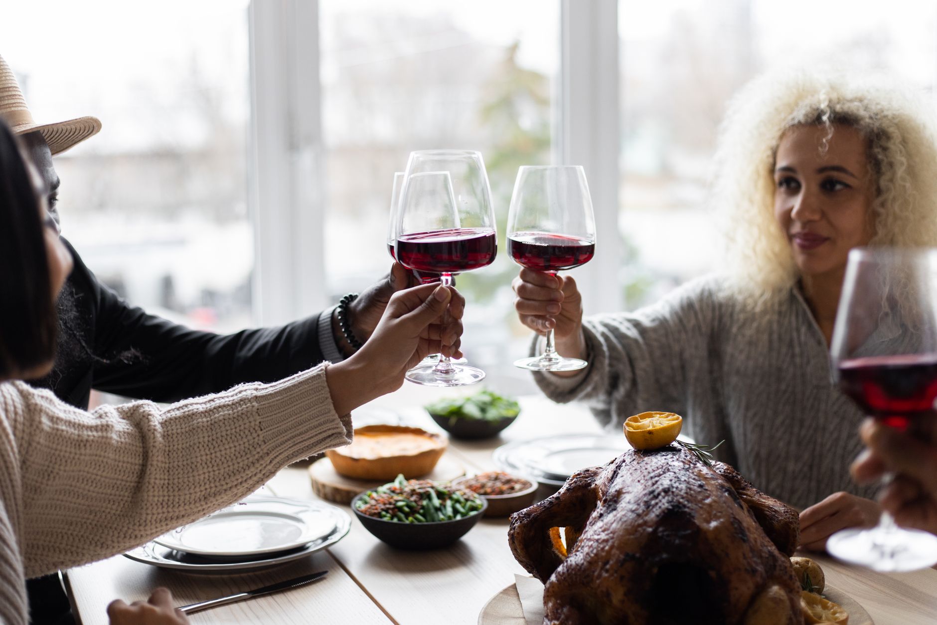 Friends toasting red wine glasses over a Thanksgiving dinner table with roasted turkey and side dishes