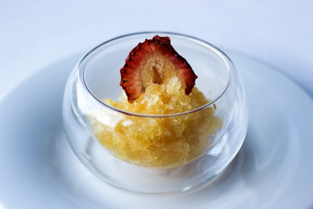 A fine dining palate cleanser, granita or sorbet served in a clear glass bowl with a dehydrated strawberry garnish on a white plate