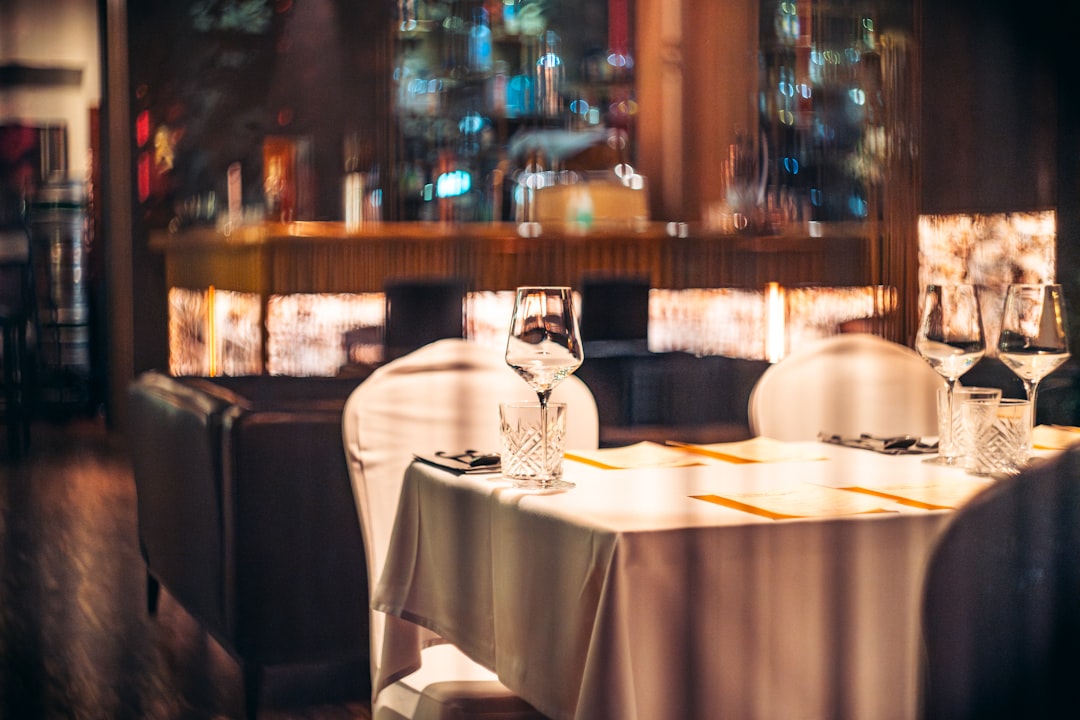 Moody fine dining restaurant interior with crystal glassware on white linen tablecloth under warm ambient lighting