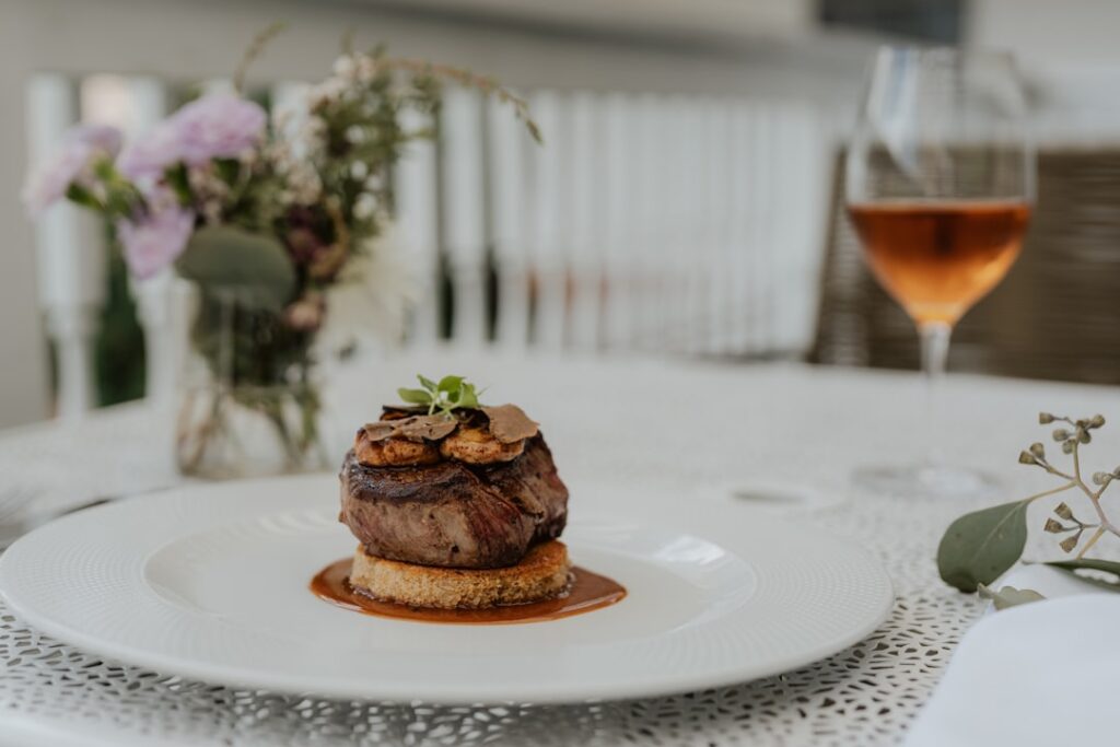 Elegantly plated filet mignon with sauce on a white plate, paired with a wine glass in the background