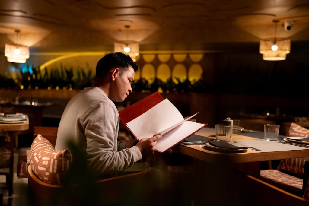 A solo diner reading a menu in a warmly lit fine dining restaurant, illustrating the anonymous inspector experience.