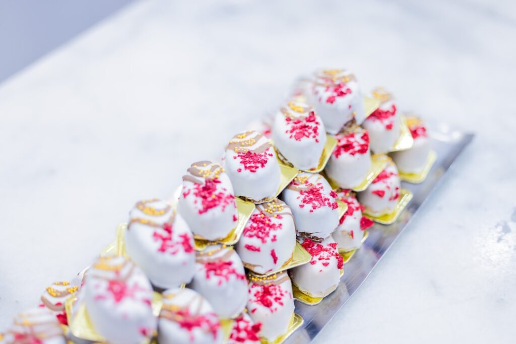 An elegant tray of small white chocolate petit fours with red sprinkles, representing mignardises served after the final course of a fine dining meal